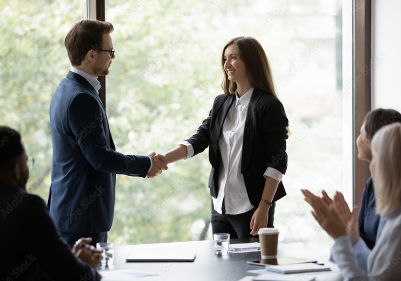 employee shaking hand with manager as employees around desk clap